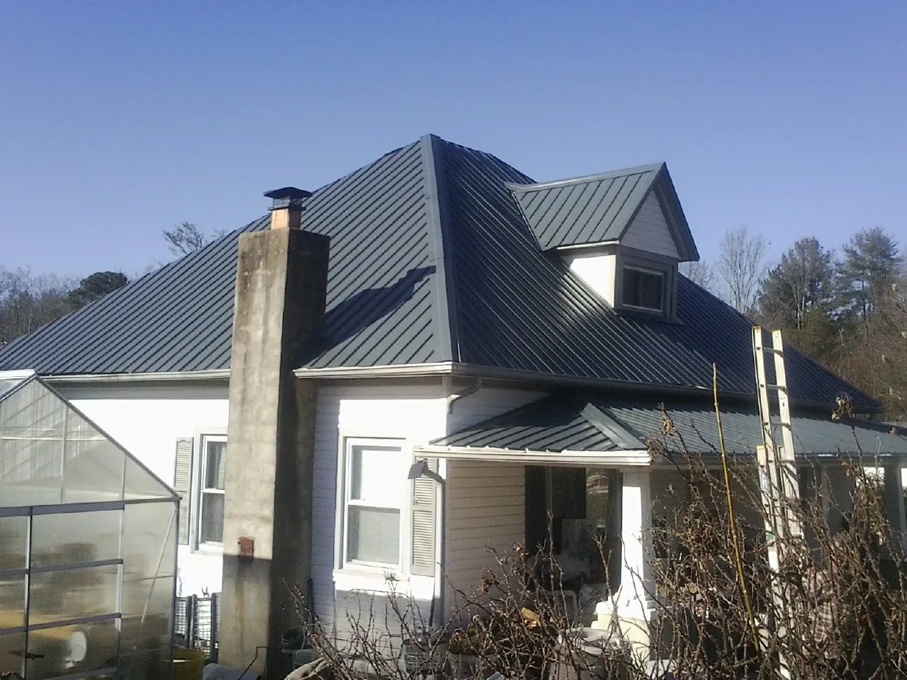 Dark blue standing seam metal roof on a white farmhouse with dormer — Slate & Tile Roof Repair by Roofing Brothers in Falconer