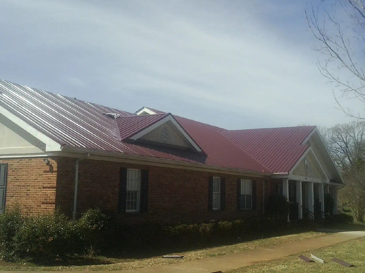 Red metal roof with gabled entries on a long brick building, from a Hail Damage Roof Repair job in Falconer