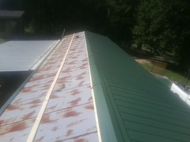 Old rusted panels beside newly installed green metal roofing — Wind Damage Roof Repair by Roofing Brothers in Falconer