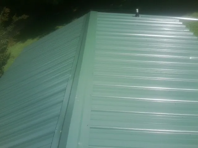 New green metal panels meeting at the ridge of a roof — Flat Roof Repair work by our crew in Falconer