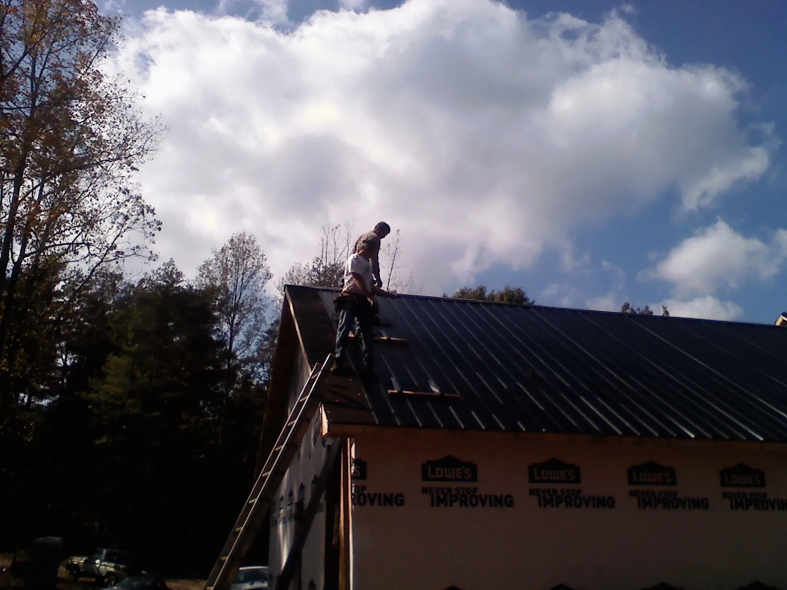 Roofer fastening dark metal panels high against a cloudy sky, from a Roof Inspection job in Falconer