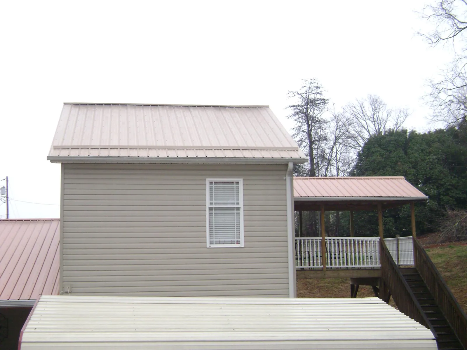 Tan metal roofs on a two story addition and attached porch, from a Roof Replacement job in Falconer